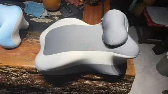A light gray multi-positional memory foam body pillow with a removable cover resting on a wooden surface.