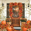 An artificial maple leaf garland in shades of orange and red decorates a doorway surrounded by pumpkins and foliage.