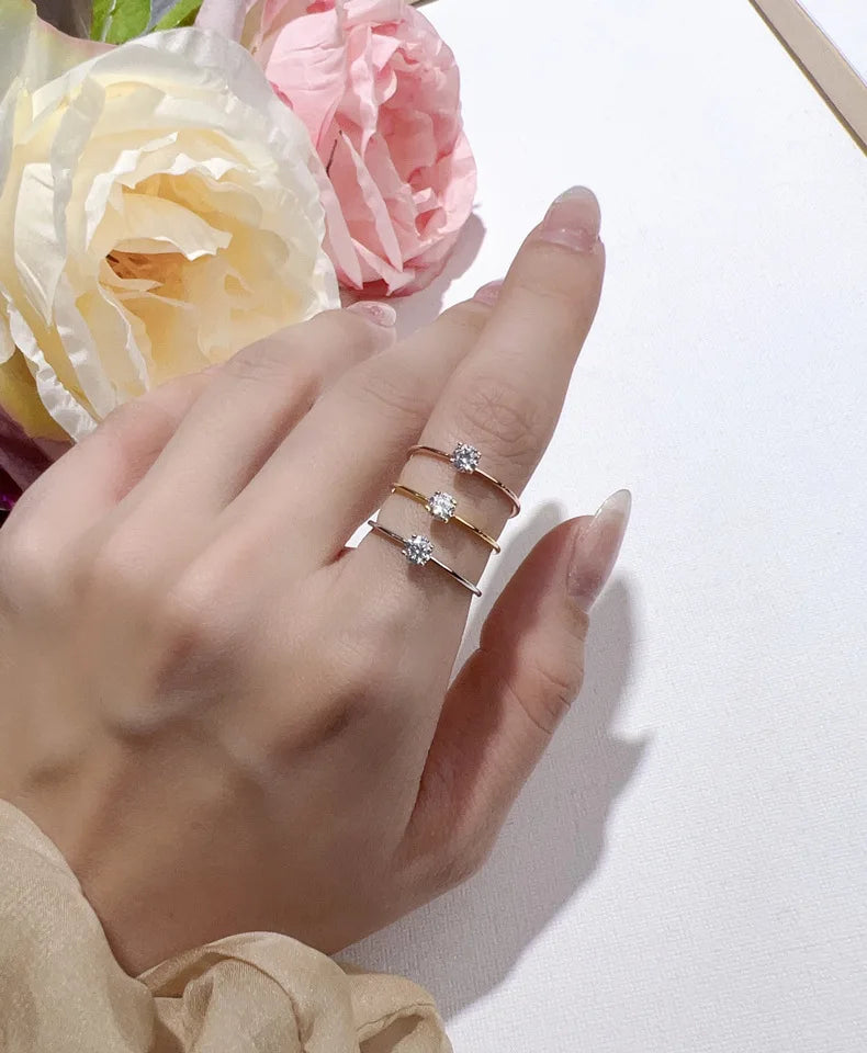 A hand wearing three minimalist moissanite solitaire rings on a white background with pink flowers.