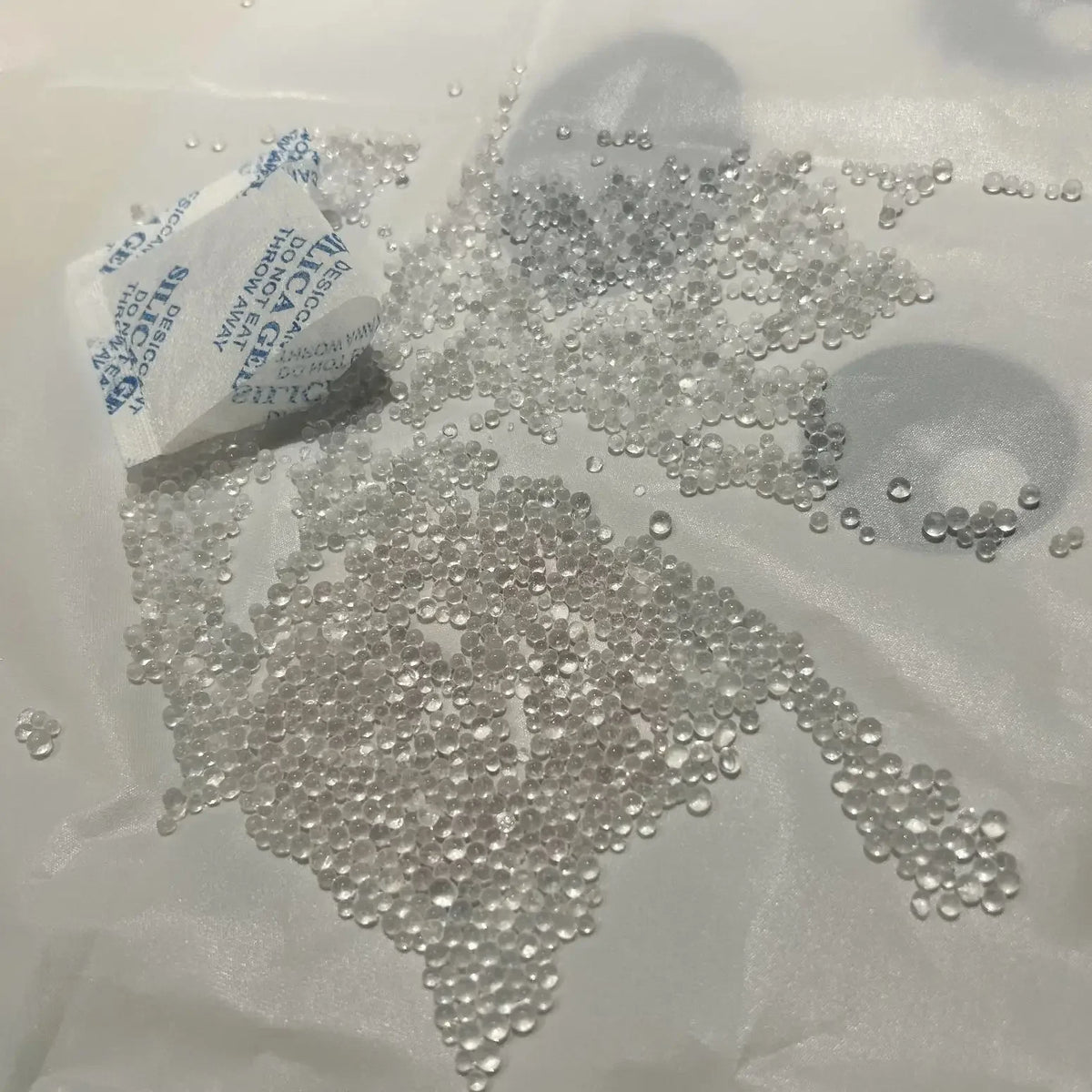 Small clear silica gel beads scattered on white paper with a label nearby.