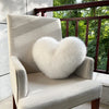 A light beige upholstered armchair with a fluffy white heart-shaped throw pillow sits on a balcony.