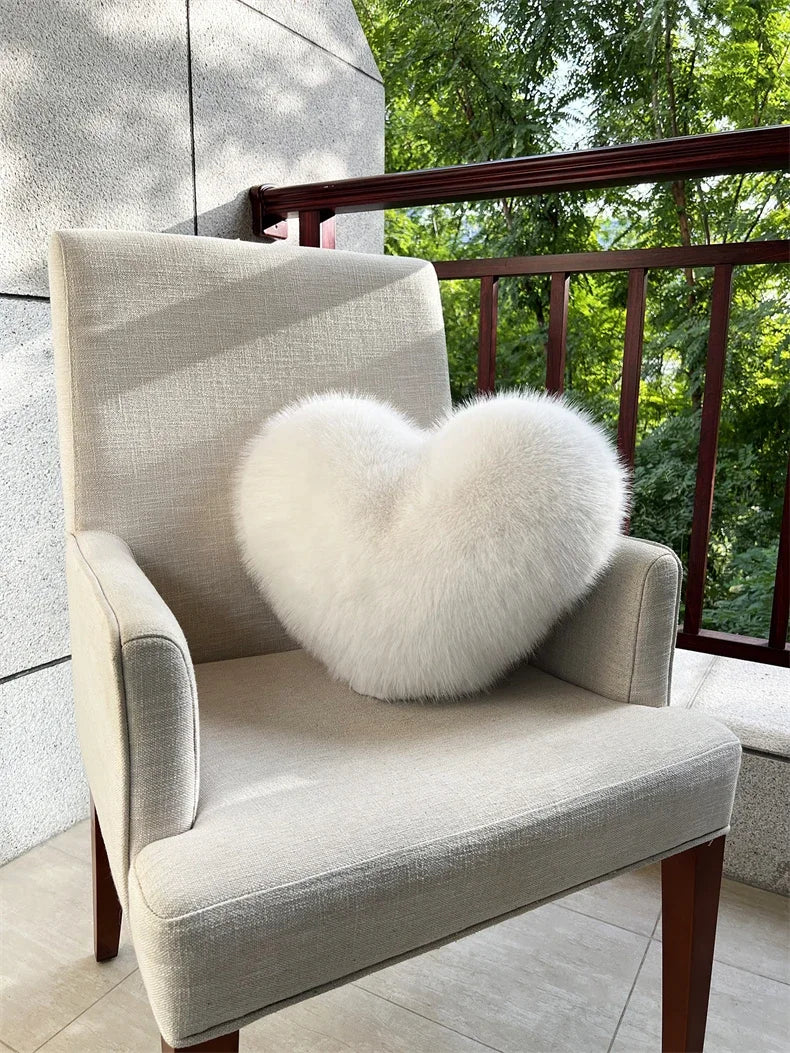 A light beige upholstered armchair with a fluffy white heart-shaped throw pillow sits on a balcony.