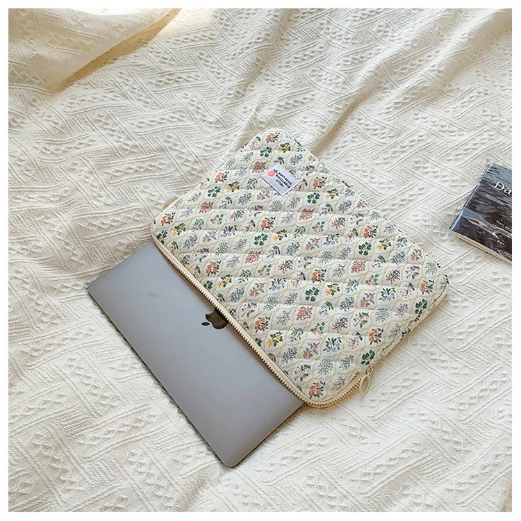 A floral printed laptop sleeve with a zipper closure resting on a cream-colored textured fabric.