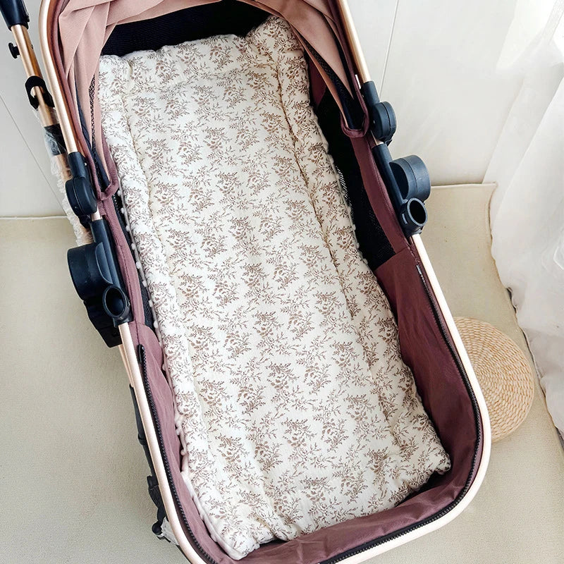 A padded baby stroller seat cushion in beige floral fabric is shown inside a pink and white carrier.