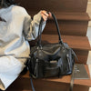 A black soft leather plaid crossbody bag with a long strap resting on dark wooden stairs.