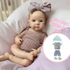 A baby reborn silicone doll wearing a knitted outfit and a bow, with an illustration of an additional outfit as a gift.