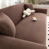 A brown stretch jacquard sofa cover featuring a textured fabric and a cream-colored decorative pillow.
