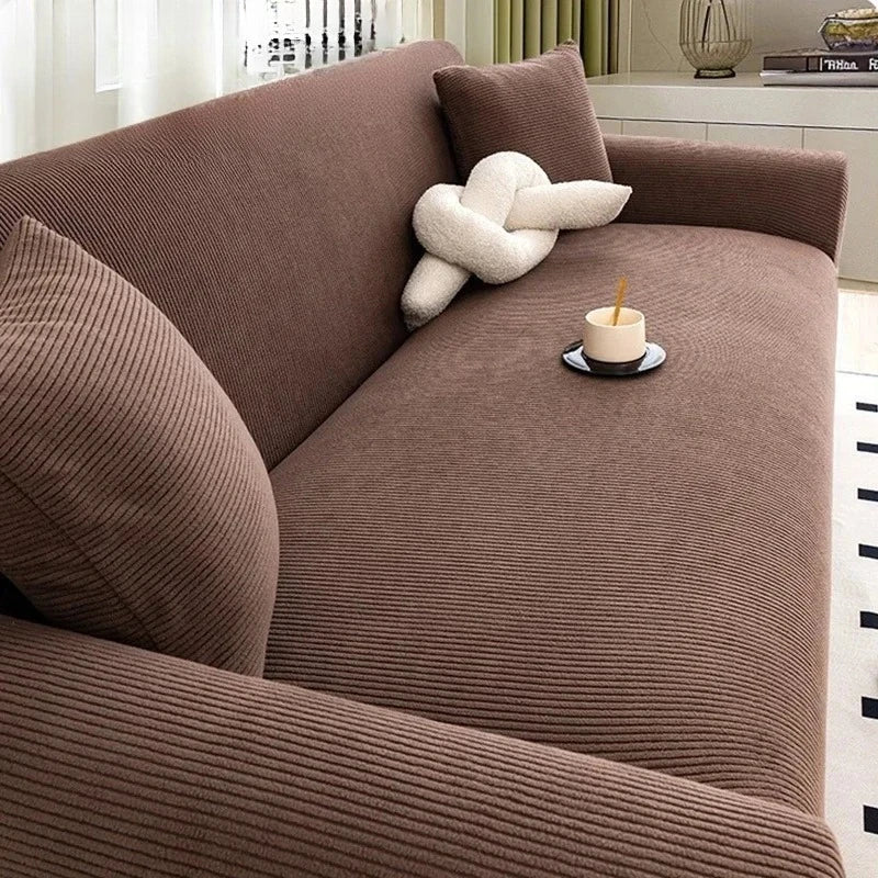 A brown stretch jacquard sofa cover featuring a textured fabric and a cream-colored decorative pillow.