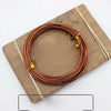 A coil of copper-toned anodized aluminum jewelry wire resting on a wooden board with twine.