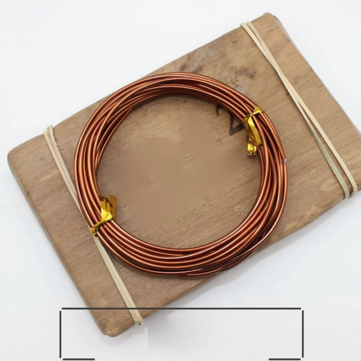 A coil of copper-toned anodized aluminum jewelry wire resting on a wooden board with twine.