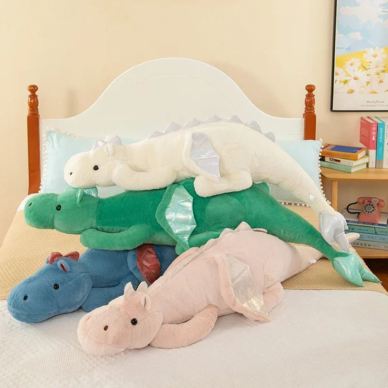 A collection of soft stuffed dragon plush pillows in white, green, and blue resting on a bed.