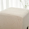 A close-up of a beige geometric jacquard stretch ottoman cover with curved lines.
