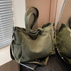 A olive green corduroy tote bag with a fabric strap is displayed next to a window.