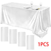 A white satin tablecloth is draped on a table set for formal dining with silverware and wine glasses.