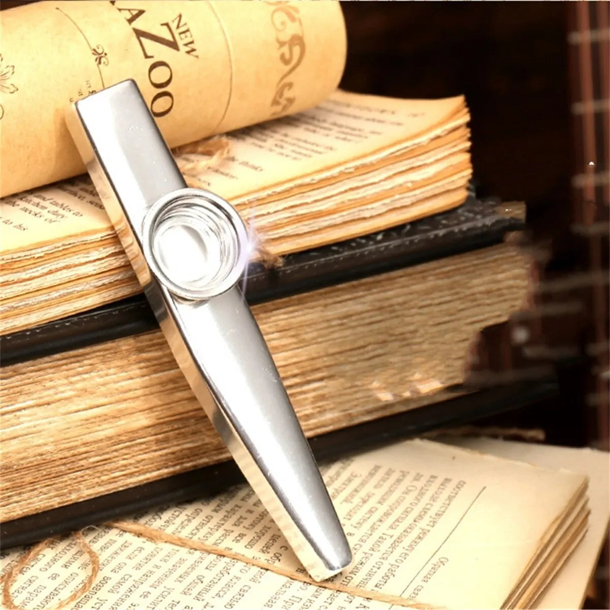 Silver aluminum kazoo with membrane diaphragm resting on a stack of old books.