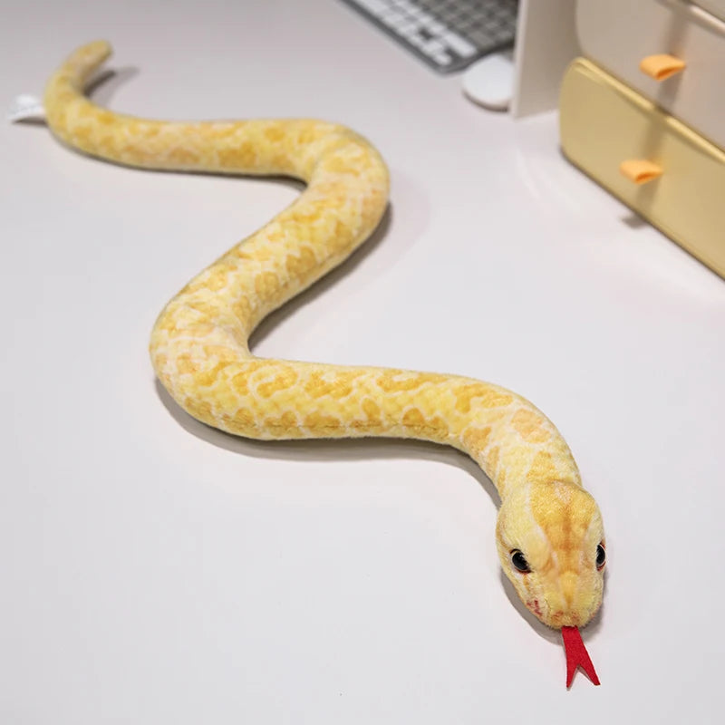 A yellow lifelike snake plush toy resembling an anaconda doll lying on a white surface.