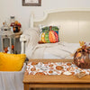 Linen table runner with a fall pumpkin and maple leaf pattern displayed on a wooden table.
