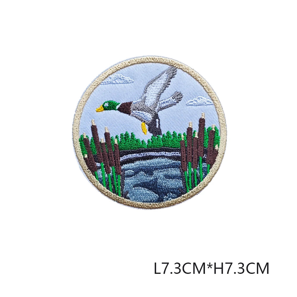 A round embroidered patch featuring a dove in flight over a landscape with reeds and water.