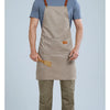 A man wearing a beige waterproof kitchen apron over a blue shirt and olive green pants.