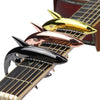A close-up of a guitar capo featuring three shark-shaped metal pieces in gold, rose gold, and black.