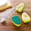 A clear dish wand with a yellow and green sponge head is shown on a wooden surface.