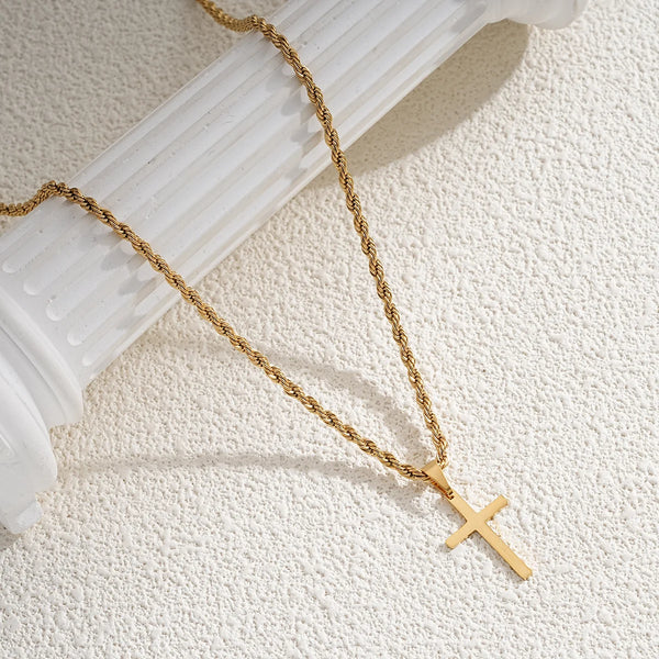 A gold-colored chain necklace with a minimalist cross pendant resting on a white marble column.