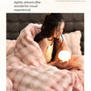 A woman is wrapped in a fluffy pink faux fur blanket indoors.