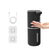 A hand is dispensing liquid from a black touchless automatic soap dispenser, with replacement parts shown nearby.