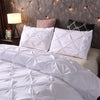 White quilted comforter and pillowcases with a pink accent pillow on a bed.
