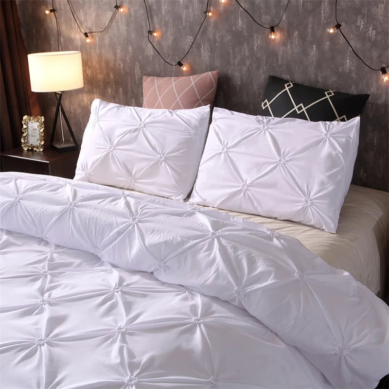 White quilted comforter and pillowcases with a pink accent pillow on a bed.