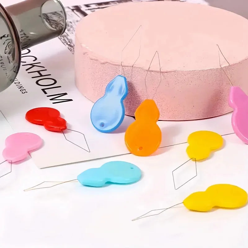 Various colored plastic needle threaders with sharp points displayed on a white surface.