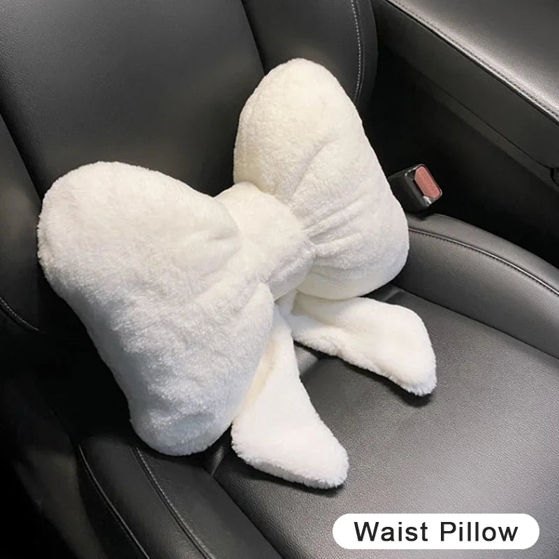A white plush bowknot waist pillow is shown resting on a dark car seat.