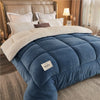 A deep blue quilted fleece blanket with a beige sherpa trim is displayed on a bed.