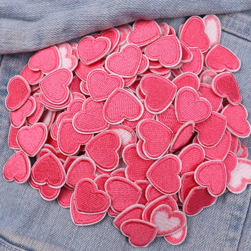 A pile of pink and white heart-shaped embroidered iron-on patches for DIY clothing decoration.