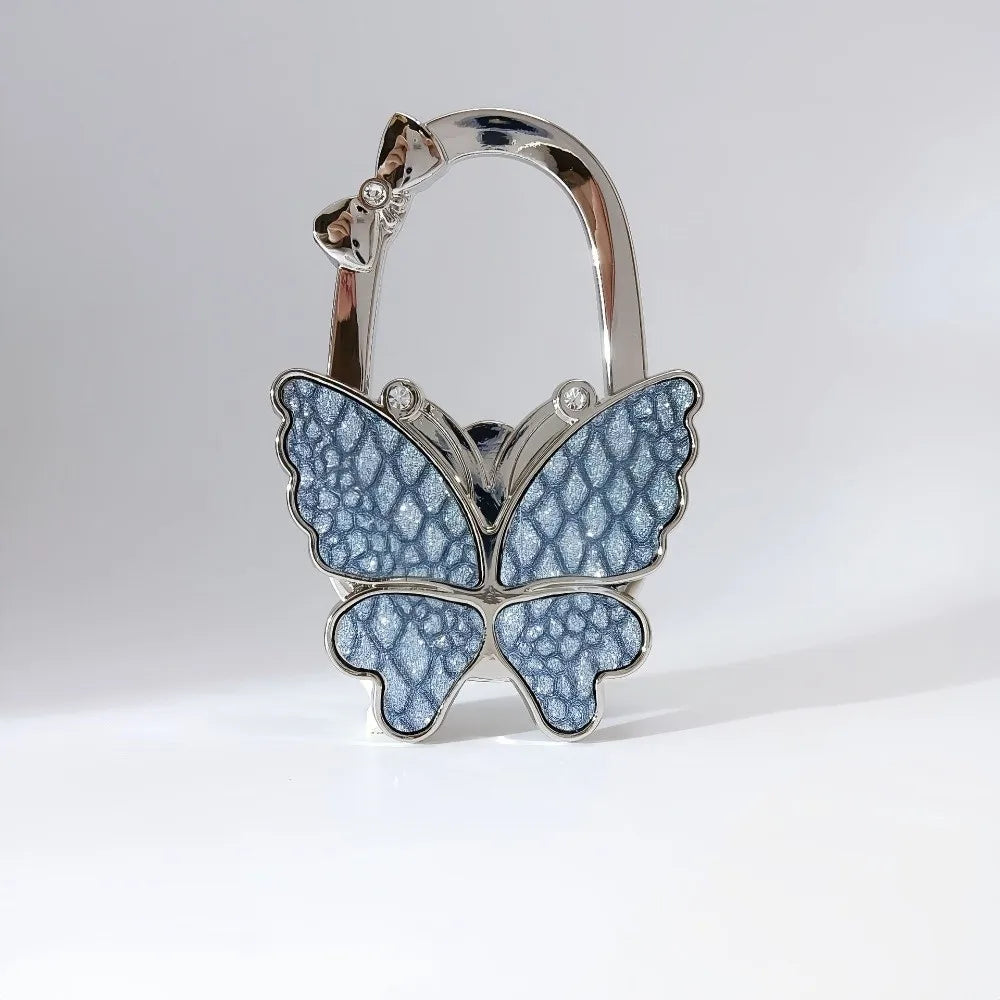 Silver foldable butterfly handbag hook with detailed texture and decorative elements.