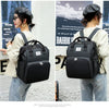 A woman wearing a beige top and jeans is holding a black large capacity diaper bag backpack.