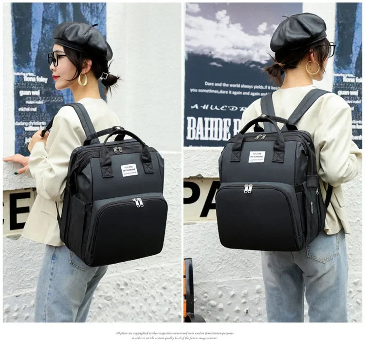 A woman wearing a beige top and jeans is holding a black large capacity diaper bag backpack.