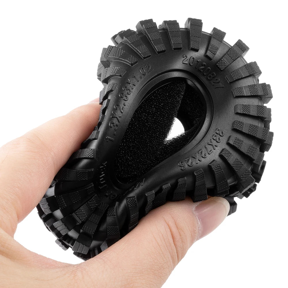 A hand holds a black mud terrain rubber tire for RC crawlers.