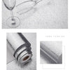 A glass wine glass is shown next to a roll of brushed silver peel-and-stick metal wallpaper.