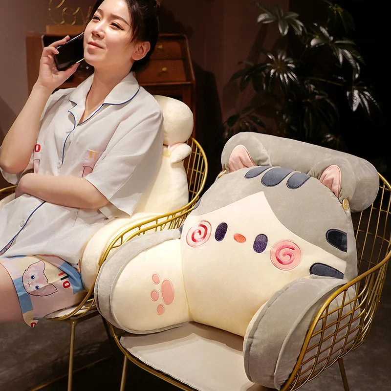 A woman is sitting in a gold-framed chair with an adorable cat and dog plush backrest cushion.