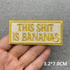 Yellow embroidered patch with the text THIS SHIT IS BANANAS on a gray fabric background