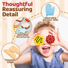 A young girl is playfully touching her eyes with wooden cookie play food structures and a kitchen mitt.