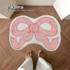 A pink bow-shaped absorbent non-slip doormat placed on a wooden floor.