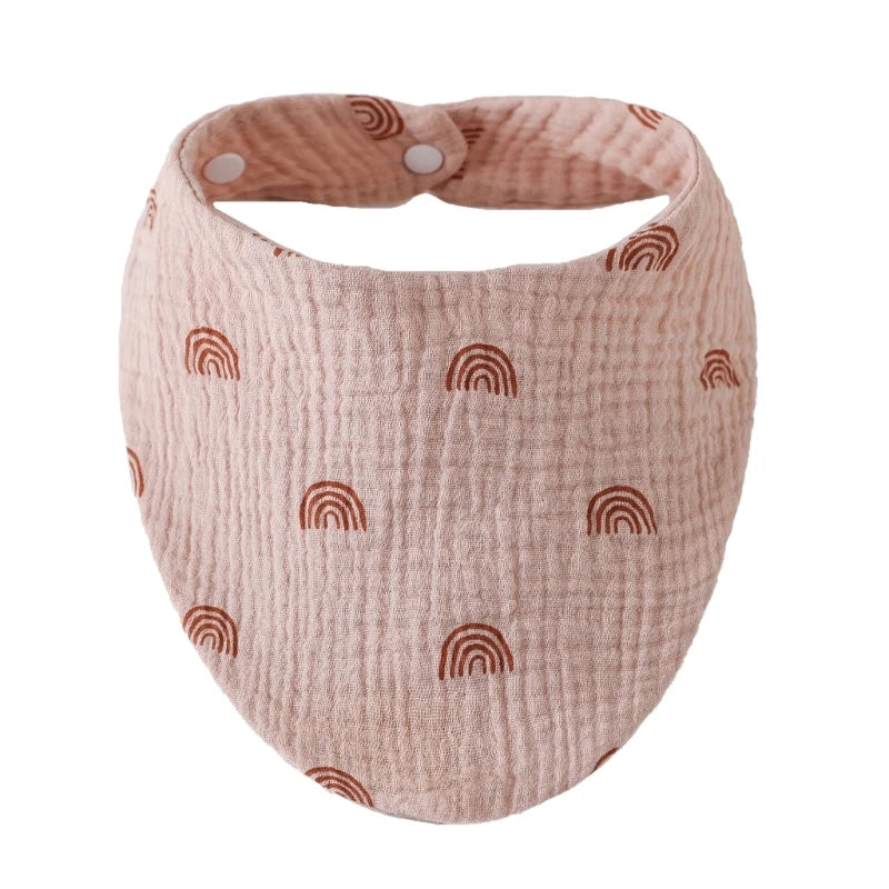 A light pink organic cotton muslin baby bib with a textured surface and a rounded shape.
