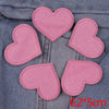 A set of five pink glitter heart and star iron-on embroidered patches laid out on a denim fabric.