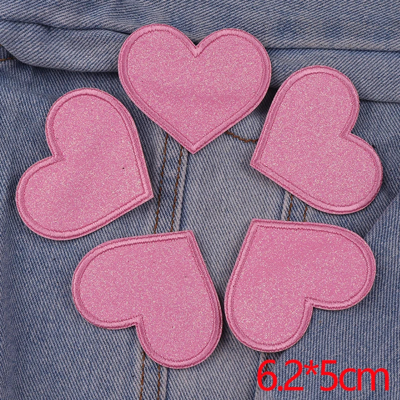 A set of five pink glitter heart and star iron-on embroidered patches laid out on a denim fabric.