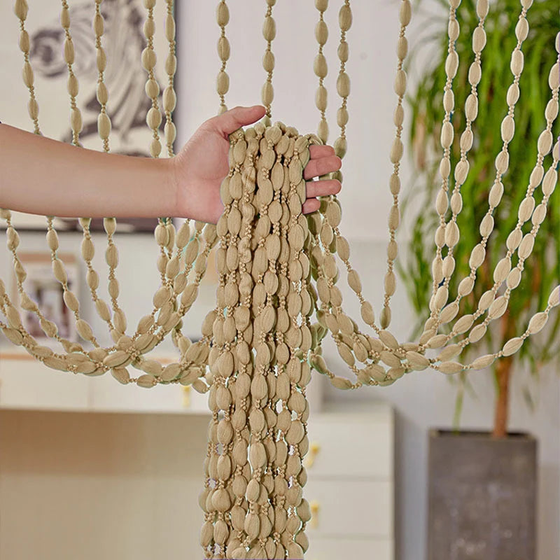 A hand is adjusting a bohemian tassel curtain made of beige fabric and small lanterns hanging from a rod.