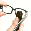 A hand holds a black eyeglasses frame and a cleaning kit with microfiber cloths and brushes.
