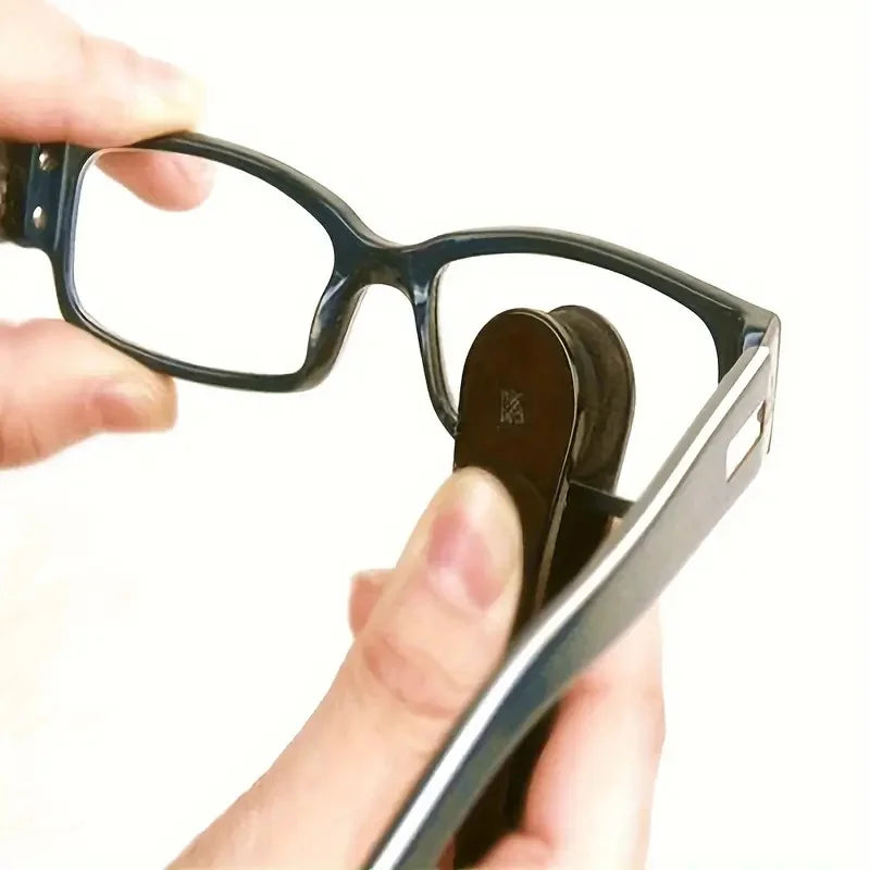 A hand holds a black eyeglasses frame and a cleaning kit with microfiber cloths and brushes.