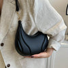 A woman holds a black textured crossbody bag with a gold chain strap against a light beige blazer.